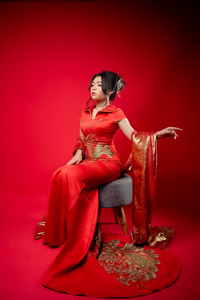 Woman in traditional red cheongsam posing elegantly in an indoor studio setting.